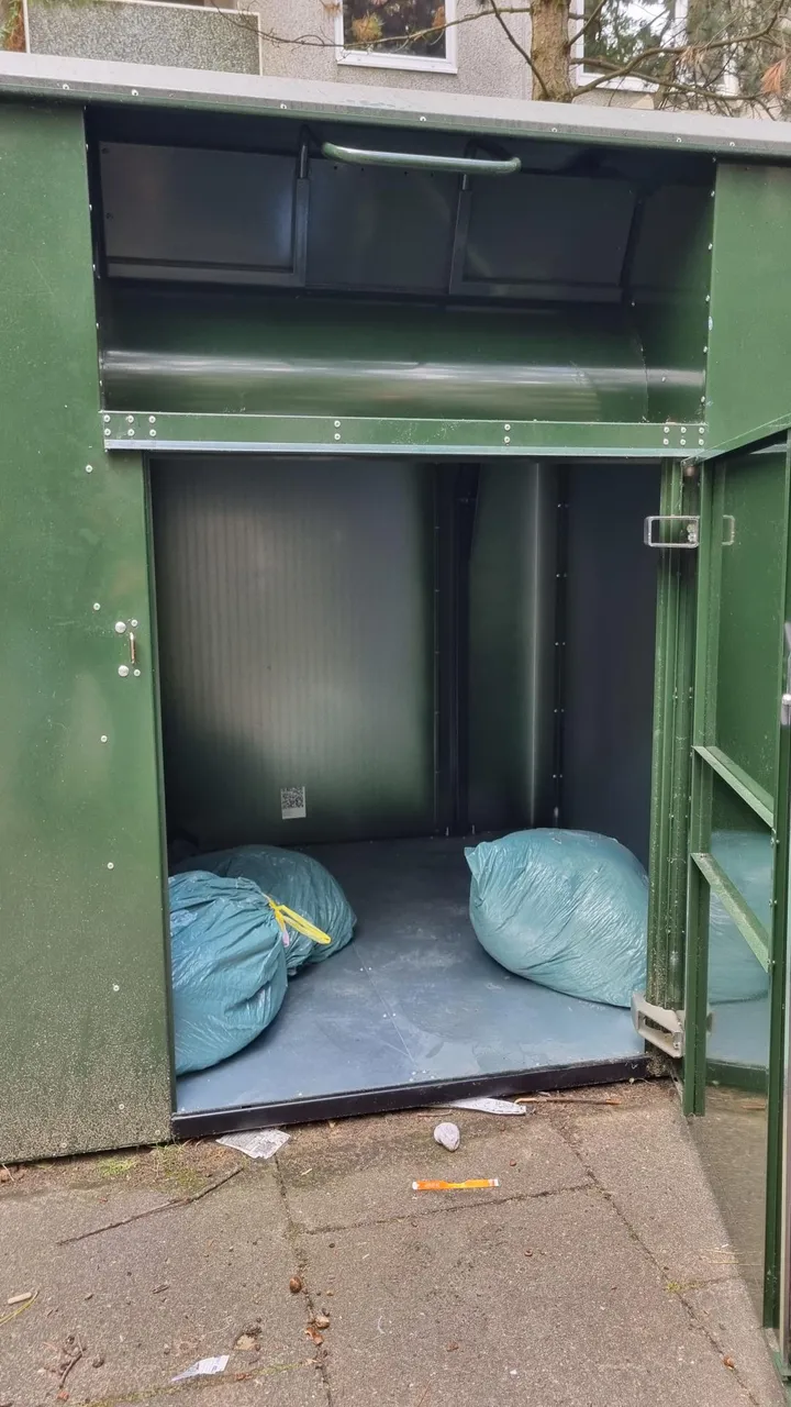 Geöffneter Altkleidercontainer der Stadtreinigung Hamburg mit Kleidersäcken und QR-Code an der Rückwand